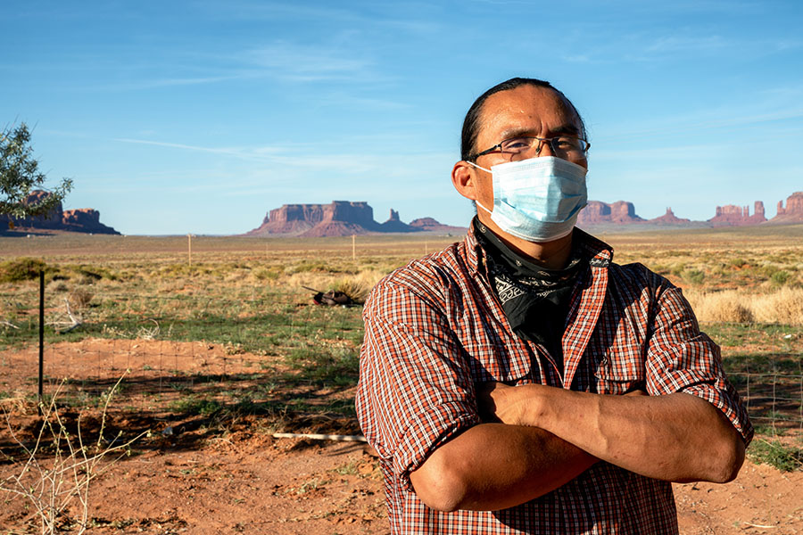 Man wearing a surgical mask standing outside with arms crossed.