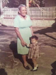 Smiling grandmother holds hands outside facing her toddler granddaughter